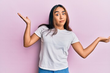 Young latin woman wearing casual white tshirt clueless and confused with open arms, no idea and doubtful face.