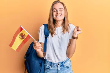 Foto op Canvas Beautiful blonde woman exchange student holding spanish flag screaming proud, celebrating victory and success very excited with raised arm © Krakenimages.com