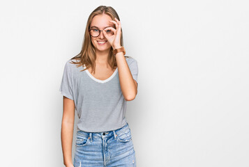 Beautiful young blonde woman wearing casual clothes and glasses doing ok gesture with hand smiling, eye looking through fingers with happy face.