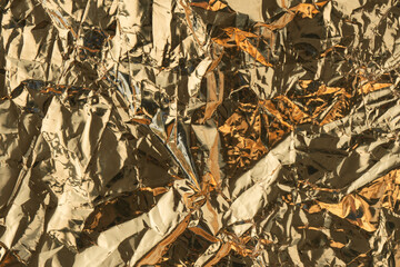 Golden crumpled shiny metallic paper. Yellow tinfoil texture for holiday. Glossy crinkled kitchen foil background. Abstract pattern of metal. Shiny wrinkled uneven surface. Wavy wrapping canvas