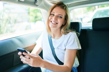 Fototapeta na wymiar Young beautiful blonde woman smiling happy sitting at the car using smartphone.