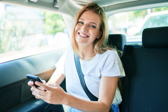 Young beautiful blonde woman smiling happy sitting at the car using smartphone.