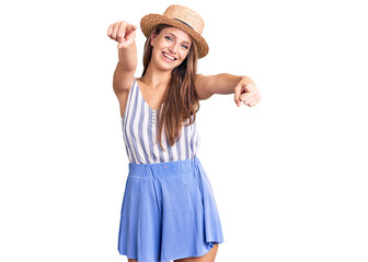 Obraz na płótnie Canvas Young beautiful blonde woman wearing summer hat pointing to you and the camera with fingers, smiling positive and cheerful