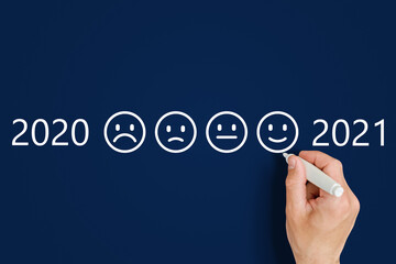male hand draws emoticons - sad and funny next to the numbers 2020 and 2021