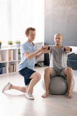 Obraz premium Young physiotherapist helping male patient to do exercise with dumbbells