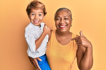 Hispanic grandson and grandmother together over yellow background smiling happy pointing with hand and finger
