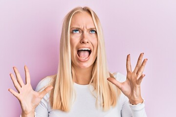 Young blonde girl wearing casual clothes crazy and mad shouting and yelling with aggressive expression and arms raised. frustration concept.