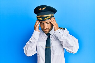 Handsome man with beard wearing airplane pilot uniform with hand on head for pain in head because stress. suffering migraine.