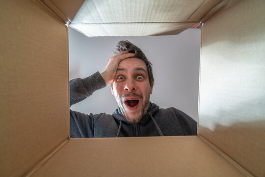 Happy and surprised man is opening a gift and looking inside cardboard box.