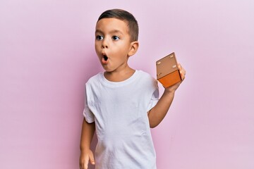 Adorable latin toddler holding gold ingot scared and amazed with open mouth for surprise, disbelief...