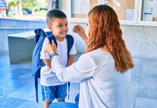 Adorable latin student boy and mom at school. Mother preparing kid putting up backpack.