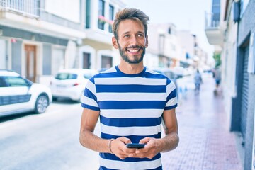 Handsome caucasian man with beard smiling happy outdoors using smartphone