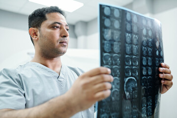 Contemporary mixed-race radiologist in uniform looking at x-ray image of patient