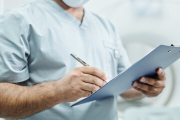 Hands of mature mixed-race male doctor in uniform making notes in document