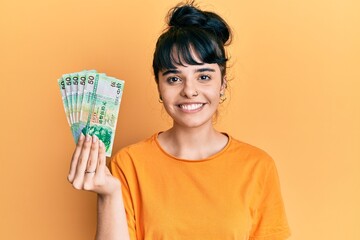 Young hispanic girl holding 50 hong kong dollars banknotes looking positive and happy standing and smiling with a confident smile showing teeth