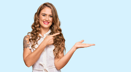 Young blonde girl wearing casual clothes amazed and smiling to the camera while presenting with hand and pointing with finger.