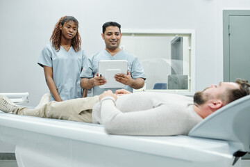 Obraz premium Young assistant and doctor in uniform standing by long couchette with patient