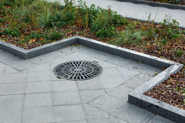 manhole cover round black metal lattice on a city park pedestrian sidewalk paved with granite gray...
