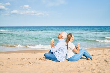 Middle age couple in love doing lotus yoga pose relaxing at the beach happy and cheerful together