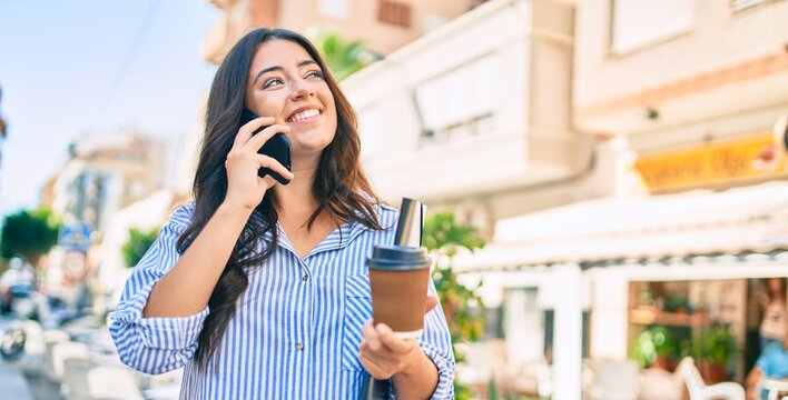 Young hispanic businesswoman talking on the smartphone and drinking take away coffee at the city.