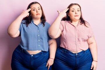 Young plus size twins wearing casual clothes shooting and killing oneself pointing hand and fingers to head like gun, suicide gesture.