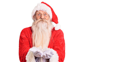 Old senior man with grey hair and long beard wearing traditional santa claus costume smiling with hands palms together receiving or giving gesture. hold and protection