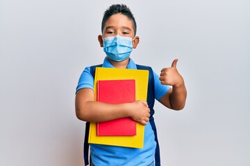 Little boy hispanic kid wearing medical mask going to school smiling happy and positive, thumb up...
