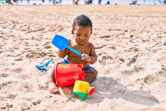 Adorable african american toddler playing with toys sitting on the sand at the beach.