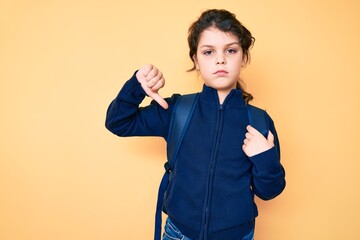 Cute hispanic child holding student backpack with angry face, negative sign showing dislike with thumbs down, rejection concept