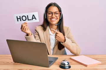 Beautiful hispanic woman wearing operator headset holding hola greenting smiling happy pointing with hand and finger © Krakenimages.com