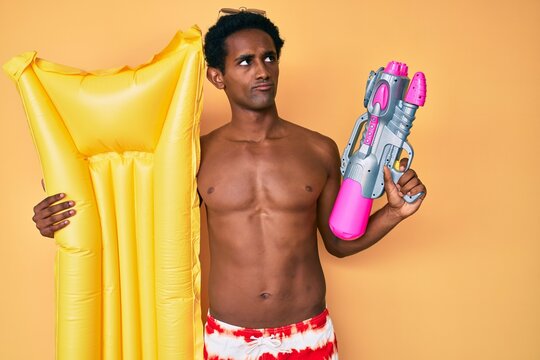 African handsome man wearing swimsuit and holding summer float smiling looking to the side and staring away thinking.
