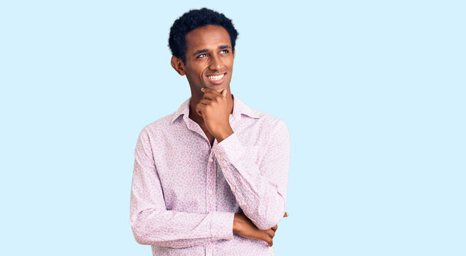 African handsome man wearing casual pink shirt with hand on chin thinking about question, pensive expression. smiling with thoughtful face. doubt concept.