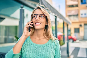 Young blonde woman smiling happy talking on the smartphone at the city.