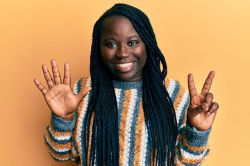 Young black woman with braids wearing casual winter sweater showing and pointing up with fingers number seven while smiling confident and happy.