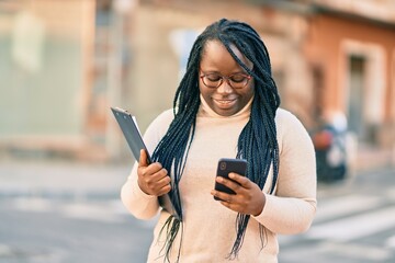 Young african american woman using smartphone and holding clipboard at the city.