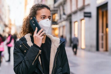 Fototapeta premium New normal. Teenager talking on the phone with a coronavirus mask. Young girl talking on the phone. Mask against covid. Teenager with face mask. Pandemic. Teenager talking.