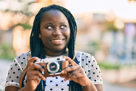 Young african american tourist woman smiling happy using vintage camera at the city.