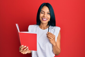 Young african american woman holding book and pencil winking looking at the camera with sexy...