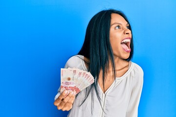 Young african american woman holding 10 colombian pesos banknotes angry and mad screaming frustrated and furious, shouting with anger. rage and aggressive concept.
