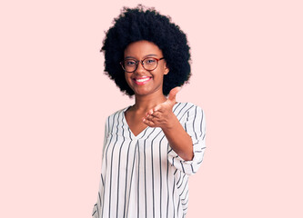 Fototapeta na wymiar Young african american woman wearing casual clothes and glasses smiling friendly offering handshake as greeting and welcoming. successful business.