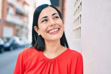 Young latin girl smiling happy leaning on the wall at the city.