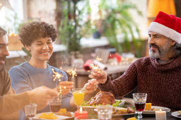 Two happy men and young woman holding bengal lights over served festive table