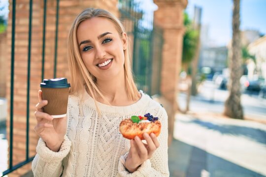 Young blonde girl smiling happy having breakfast standing at the city.