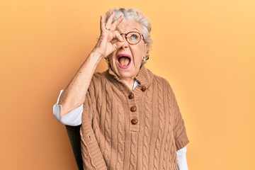 Senior grey-haired woman doing ok positive gesture on eye angry and mad screaming frustrated and...