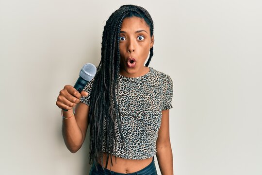 African american woman singing song using microphone scared and amazed with open mouth for surprise, disbelief face