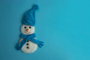 Christmas concept. Handmade snowman with snow, scarf, hat and carrot on a light blue background....