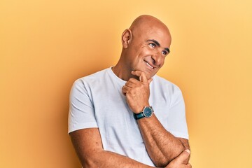 Mature middle east man wearing casual white tshirt with hand on chin thinking about question, pensive expression. smiling with thoughtful face. doubt concept.