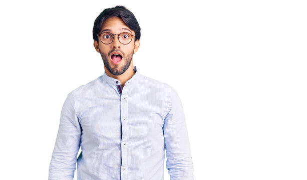 Handsome hispanic man wearing business shirt and glasses in shock face, looking skeptical and sarcastic, surprised with open mouth