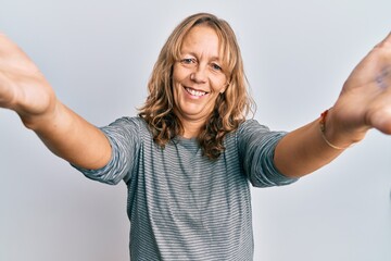 Middle age blonde woman wearing casual clothes looking at the camera smiling with open arms for hug. cheerful expression embracing happiness.