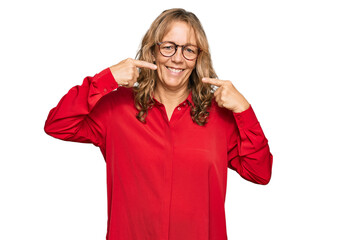 Middle age blonde woman wearing casual shirt over red background smiling cheerful showing and pointing with fingers teeth and mouth. dental health concept.